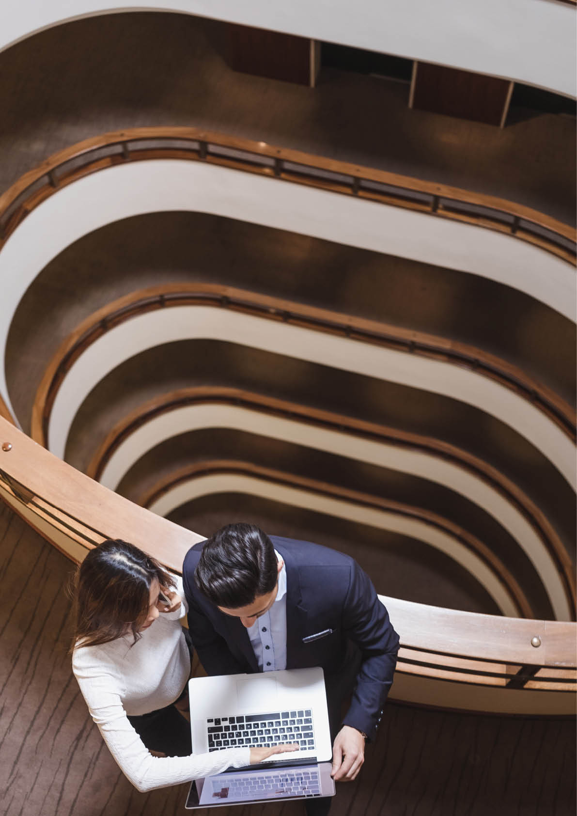 Business People Standing in the Middle of a Building's Corridor, Discussing and Using Laptop
